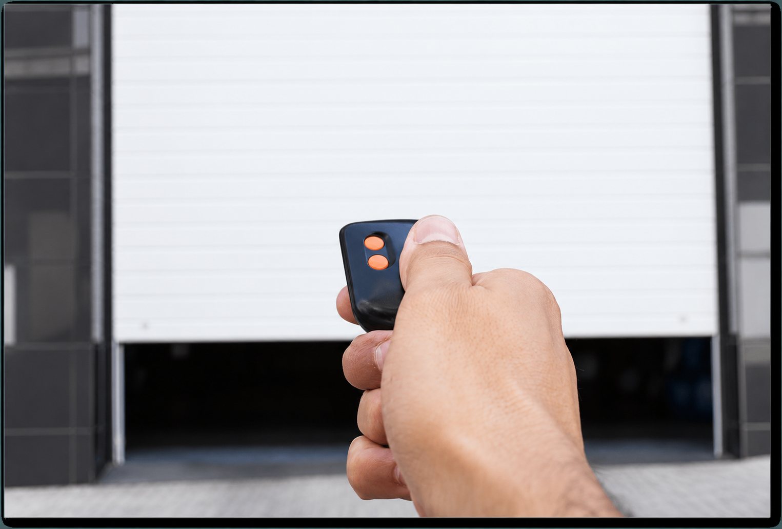 Une main pointe une petite télécommande noire à deux boutons orange vers une porte de garage blanche qui s’ouvre.
